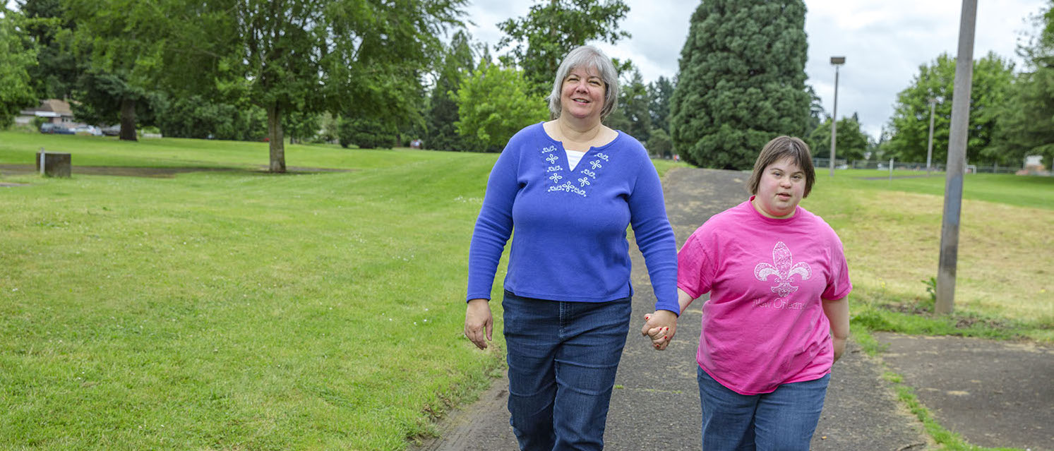 Homecare worker walking and holding hands with her daughter who is also her client
